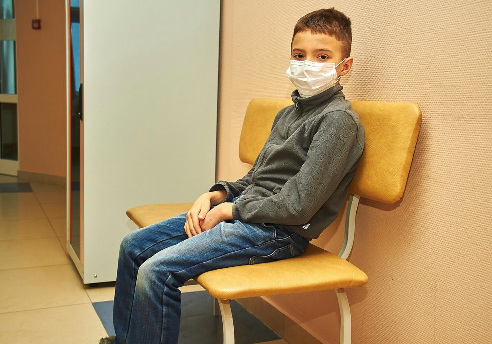 待合室で静かに過ごすマスク姿の男の子